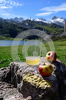 Glass of natural Asturian cider made fromÂ fermented apples with view on Covadonga lake and tops of Picos de Europa mountains,